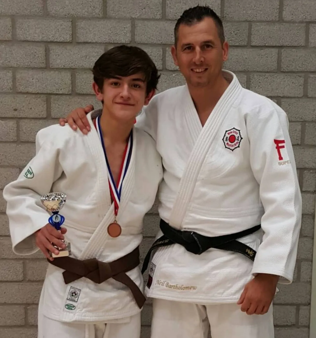 Neil with a junior judoka holding a medal and trophy after a competition in Holland